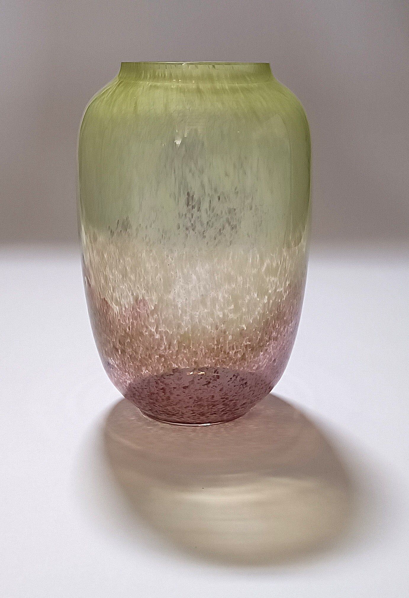 Vaso verde e rosa com efeito espuma, fotografado com sombra projetada no fundo branco.